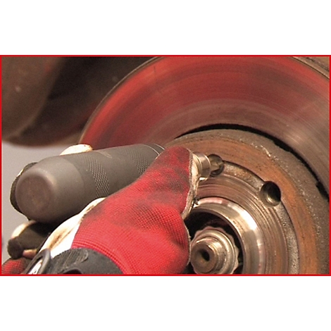 Person hält Werkzeug an einer Bremsscheibe. Roter Handschuh. Metall, Rost, Schraube.